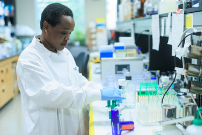 woman in white coat wearing blue gloves working at a lab bench