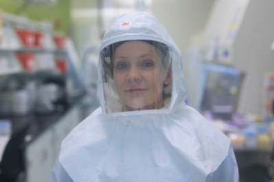 woman in PPE hood with clear mask looking at camera