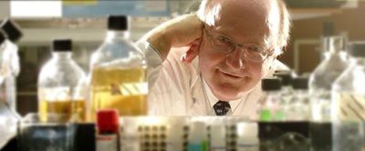 man in lab coat looking through shelf of medical supplies towards camera