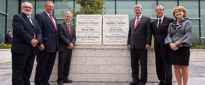 politicians in suits beside cornerstone with dedication text looking at camera