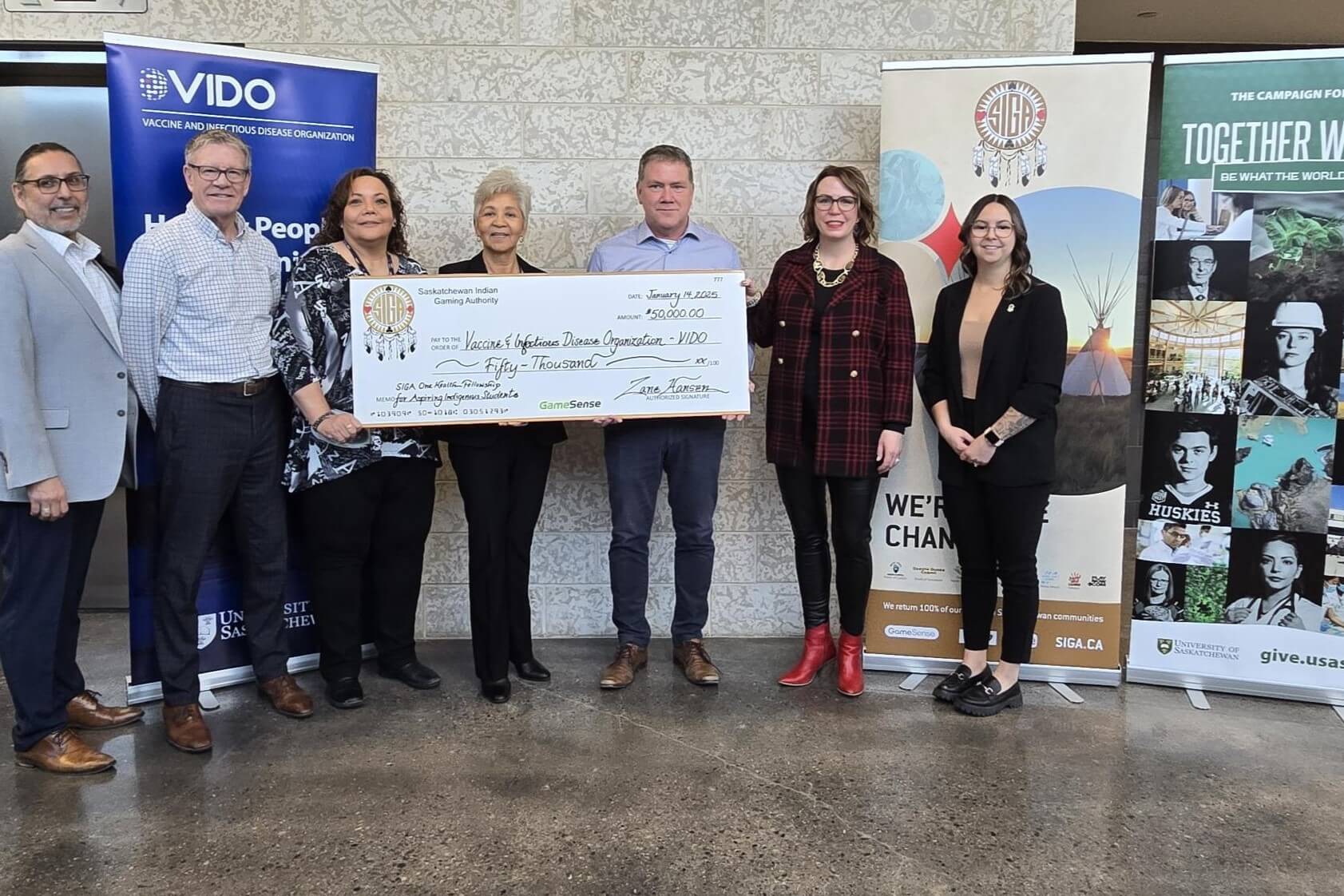 a group of people holding a giant cheque for $50,000 with three organization banners behind them